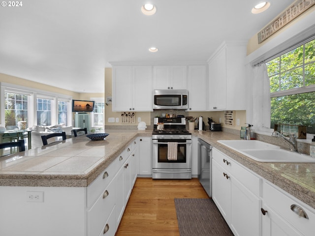 kitchen featuring sink, light wood-type flooring, white cabinetry, plenty of natural light, and stainless steel appliances