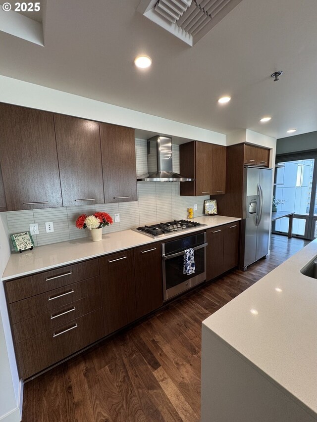 kitchen with dark hardwood / wood-style floors, sink, a kitchen island with sink, appliances with stainless steel finishes, and wall chimney exhaust hood