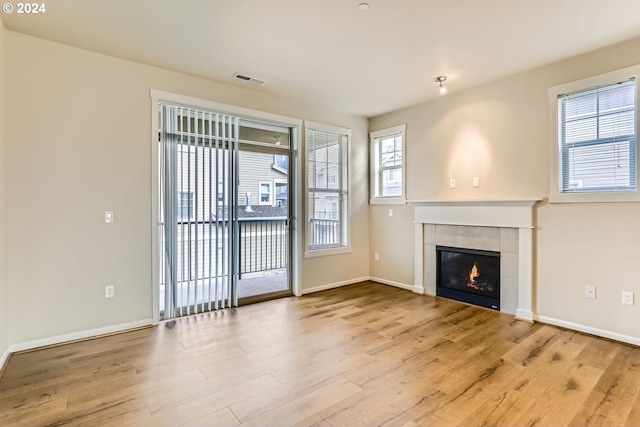 unfurnished living room featuring a tile fireplace, a healthy amount of sunlight, and light hardwood / wood-style floors