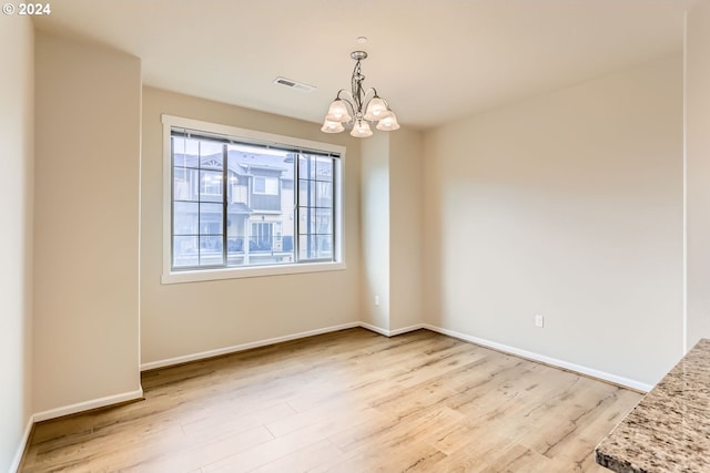 spare room with light hardwood / wood-style flooring and a notable chandelier