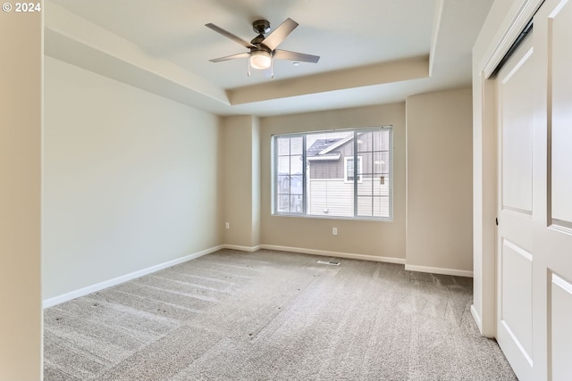 unfurnished bedroom with light carpet, a closet, a raised ceiling, and ceiling fan