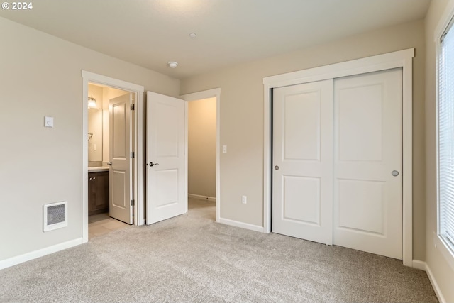 unfurnished bedroom featuring multiple windows, light carpet, a closet, and ensuite bath