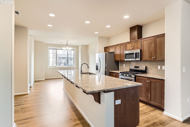 kitchen featuring an inviting chandelier, sink, light wood-type flooring, an island with sink, and appliances with stainless steel finishes