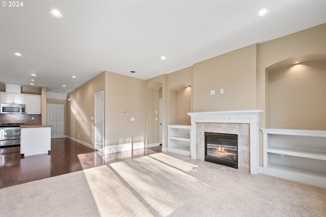 unfurnished living room with built in shelves, carpet, and a tiled fireplace