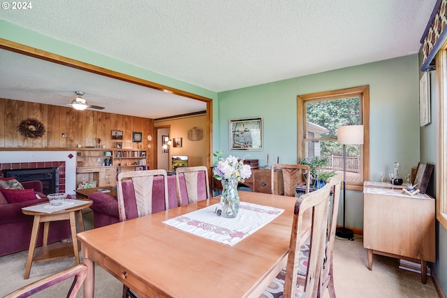 carpeted dining space featuring ceiling fan, a tiled fireplace, and a textured ceiling