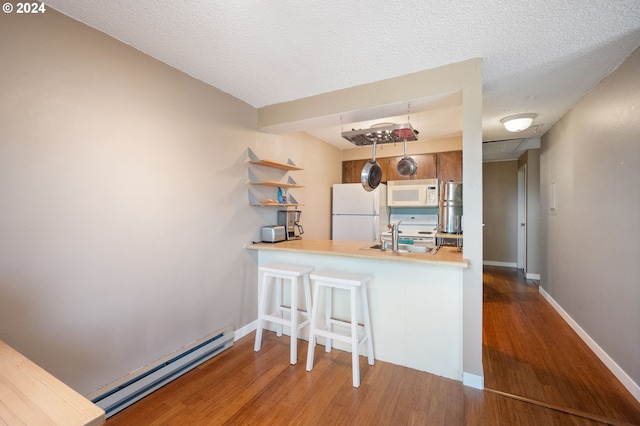 kitchen featuring a baseboard radiator, hardwood / wood-style floors, kitchen peninsula, and white appliances