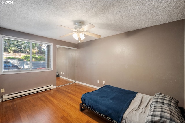 bedroom with a closet, baseboard heating, hardwood / wood-style floors, a textured ceiling, and ceiling fan