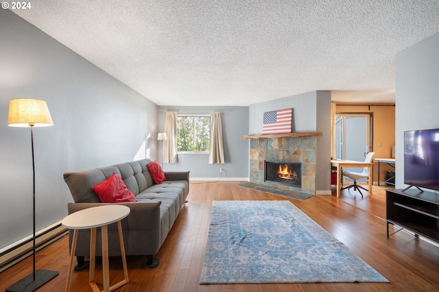 living room with hardwood / wood-style flooring, a textured ceiling, a baseboard heating unit, and a tile fireplace