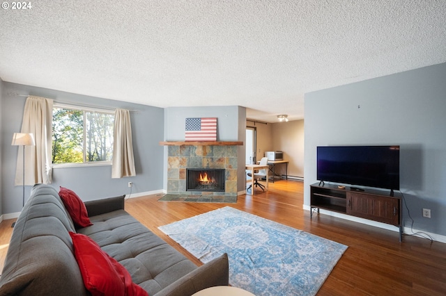 living room featuring a textured ceiling, a baseboard heating unit, hardwood / wood-style flooring, and a tile fireplace