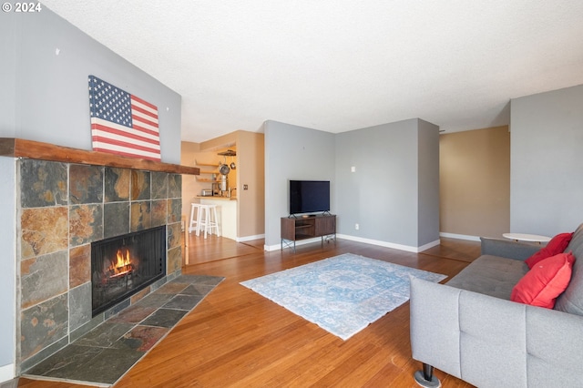 living room with a textured ceiling, hardwood / wood-style flooring, and a tiled fireplace