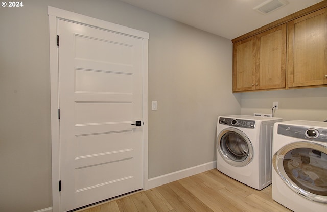 laundry area with cabinets, light wood-type flooring, and washing machine and clothes dryer