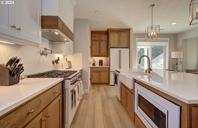 kitchen featuring sink, range with gas cooktop, stainless steel microwave, an island with sink, and custom range hood