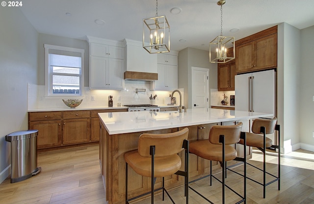 kitchen with decorative light fixtures, sink, white cabinets, custom exhaust hood, and a kitchen island with sink