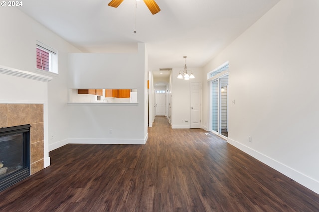 unfurnished living room featuring a fireplace, dark wood-type flooring, and ceiling fan with notable chandelier