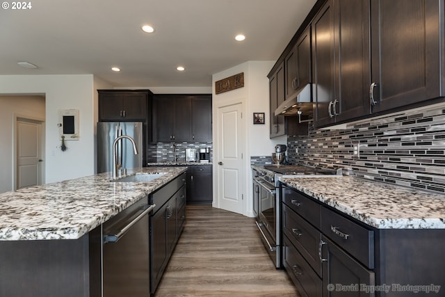 kitchen with sink, an island with sink, stainless steel appliances, light hardwood / wood-style floors, and decorative backsplash