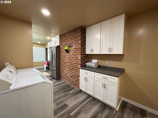 clothes washing area featuring independent washer and dryer, dark hardwood / wood-style flooring, and brick wall