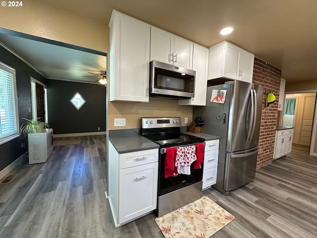 kitchen featuring stainless steel appliances, white cabinetry, dark hardwood / wood-style floors, and brick wall