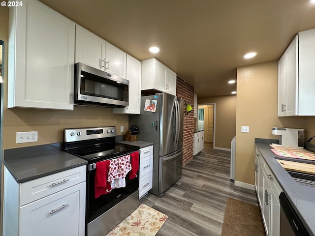 kitchen featuring dark hardwood / wood-style floors, white cabinetry, stainless steel appliances, and brick wall