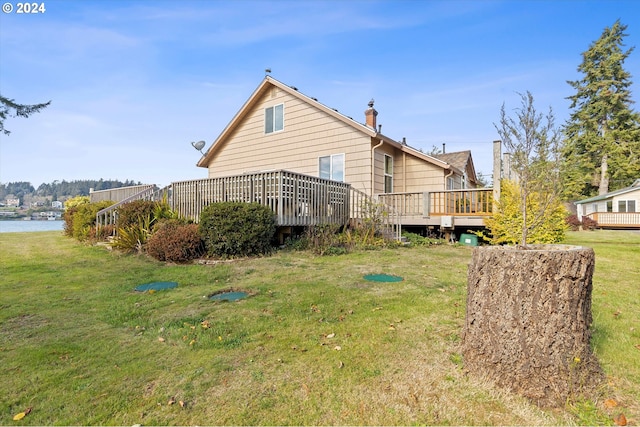 back of house with a deck with water view and a lawn