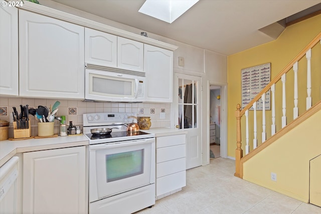 kitchen with white cabinets, backsplash, light tile patterned flooring, a skylight, and white appliances