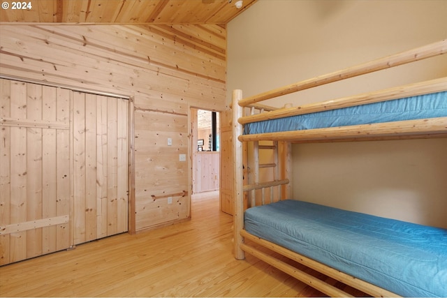 unfurnished bedroom with vaulted ceiling, wood walls, and light wood-type flooring