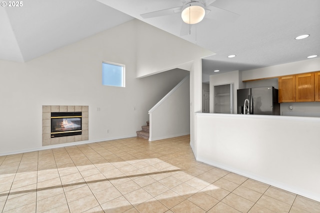 unfurnished living room with ceiling fan, lofted ceiling, a fireplace, and light tile patterned floors