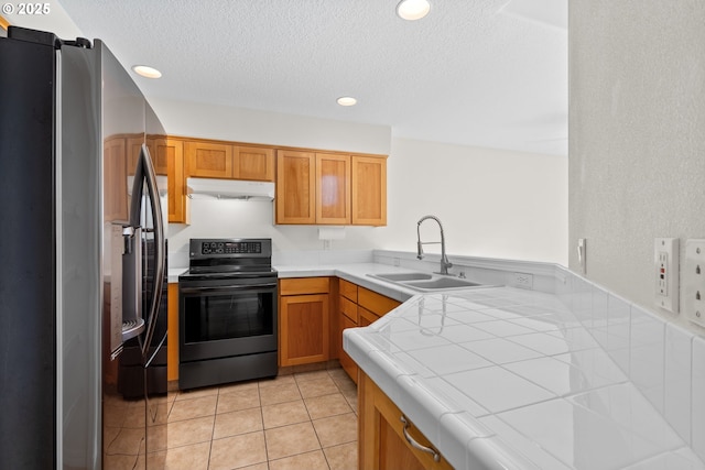 kitchen with sink, black range with electric cooktop, light tile patterned flooring, stainless steel fridge with ice dispenser, and tile countertops