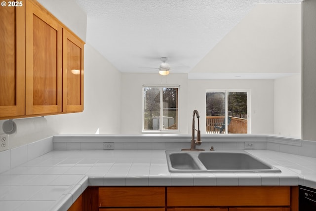 kitchen with sink, tile counters, dishwasher, and ceiling fan