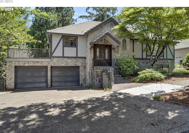 english style home featuring a garage, concrete driveway, stone siding, a tile roof, and stucco siding