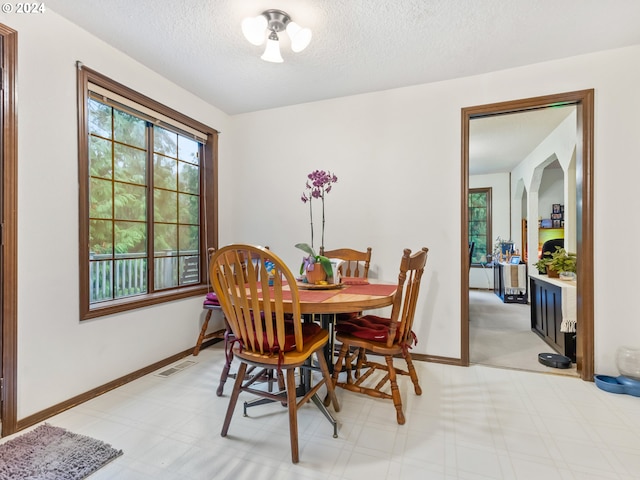 dining room featuring light floors, baseboards, visible vents, and a textured ceiling