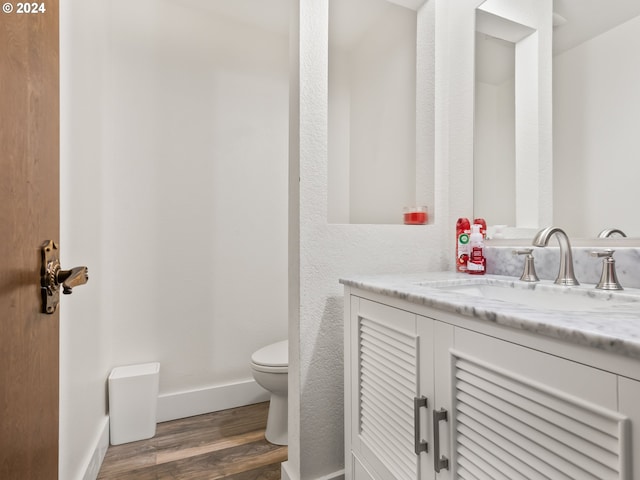 half bathroom featuring toilet, vanity, baseboards, and wood finished floors