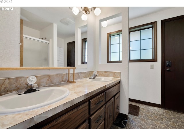 full bathroom featuring double vanity, a sink, a shower with door, and baseboards