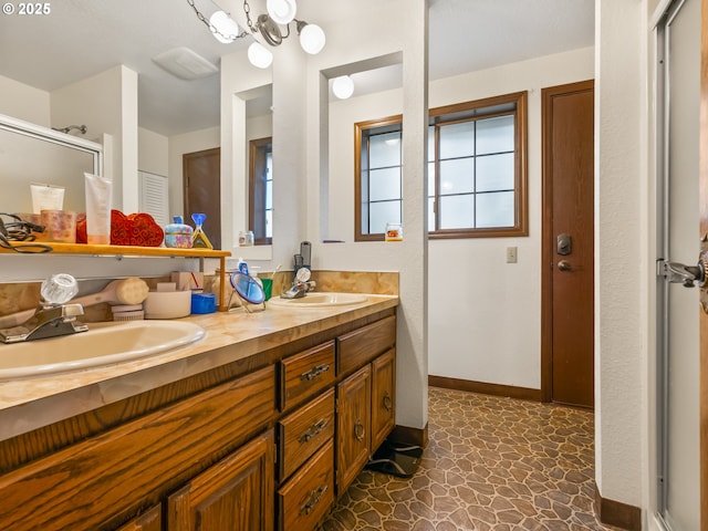 bathroom featuring a chandelier, double vanity, a sink, and baseboards