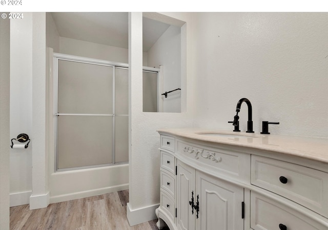 bathroom with baseboards, combined bath / shower with glass door, wood finished floors, and vanity