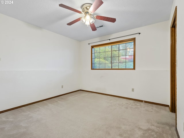 spare room featuring a ceiling fan, light colored carpet, visible vents, and a textured ceiling