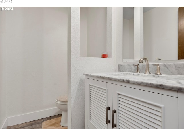 half bath featuring toilet, wood finished floors, vanity, and baseboards