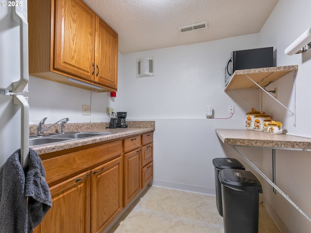 kitchen with a textured ceiling, a sink, visible vents, light countertops, and brown cabinetry