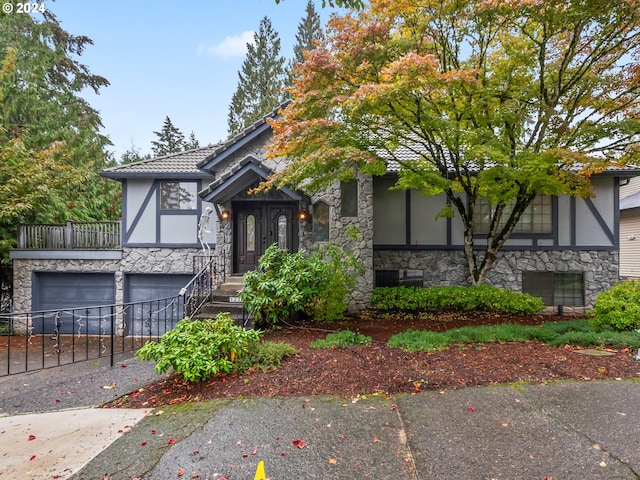 tudor house with a garage, stone siding, driveway, and stucco siding