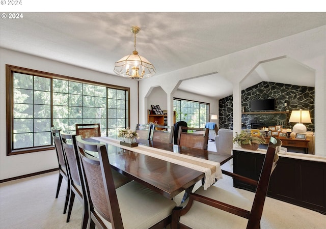 dining space featuring light carpet, baseboards, lofted ceiling, a fireplace, and a chandelier