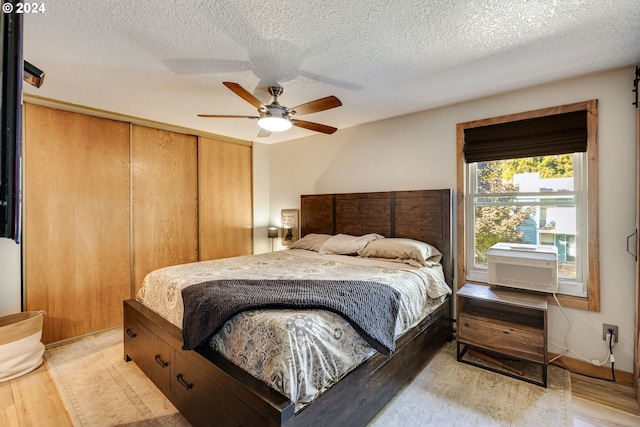 bedroom featuring light wood-type flooring, ceiling fan, cooling unit, and a textured ceiling