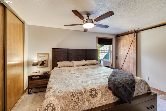 bedroom featuring ceiling fan, a barn door, light hardwood / wood-style floors, and a textured ceiling