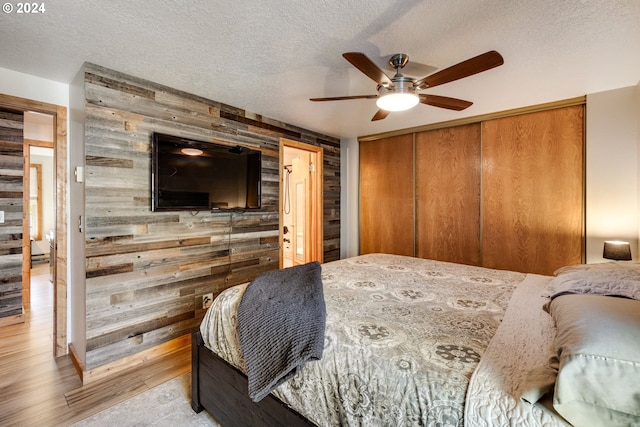 bedroom with a textured ceiling, wooden walls, a closet, and ceiling fan