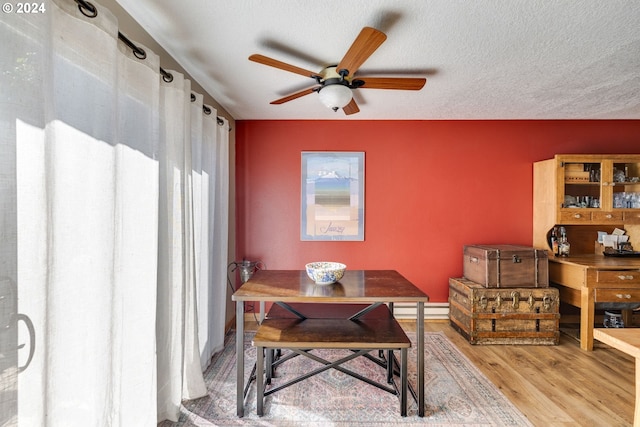 dining space featuring wood-type flooring, baseboard heating, a textured ceiling, and ceiling fan