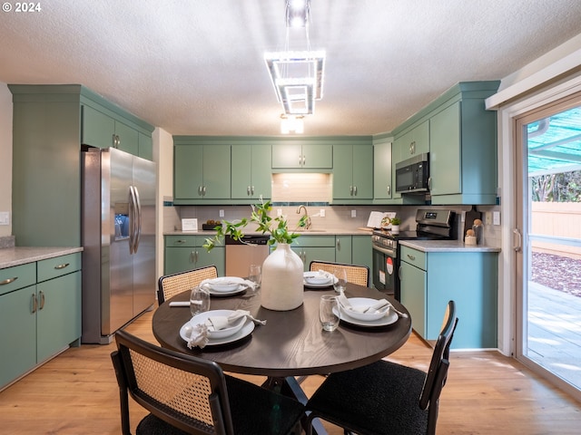 kitchen with a textured ceiling, green cabinets, stainless steel appliances, light hardwood / wood-style floors, and decorative backsplash