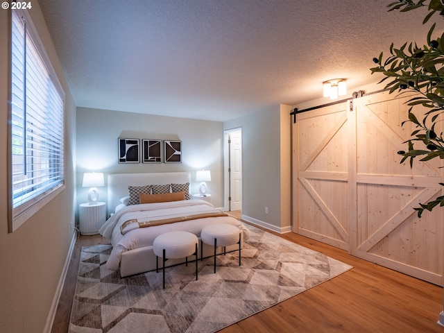 bedroom featuring wood-type flooring, a textured ceiling, and a barn door