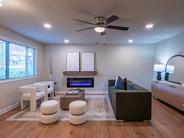 living room featuring light hardwood / wood-style floors, ceiling fan, and a textured ceiling