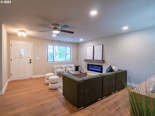 living room featuring light hardwood / wood-style floors, ceiling fan, and a textured ceiling