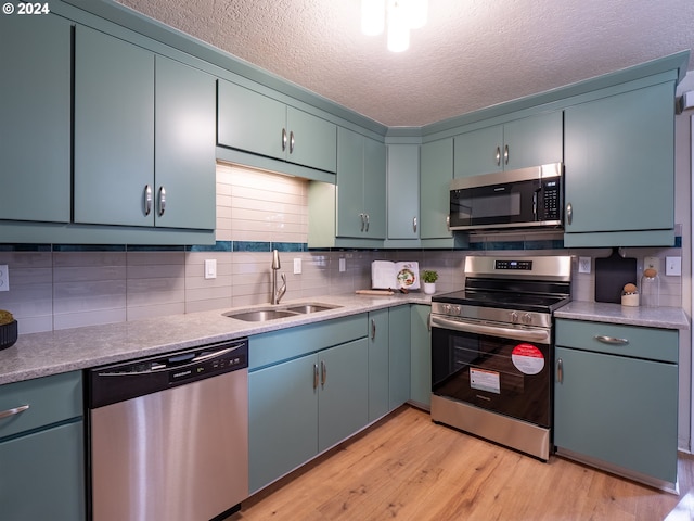 kitchen with a textured ceiling, light hardwood / wood-style floors, tasteful backsplash, appliances with stainless steel finishes, and sink