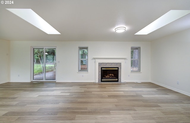 unfurnished living room featuring lofted ceiling with skylight, wood finished floors, baseboards, and a high end fireplace