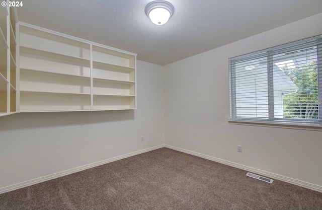 spare room with visible vents, dark carpet, a textured ceiling, and baseboards